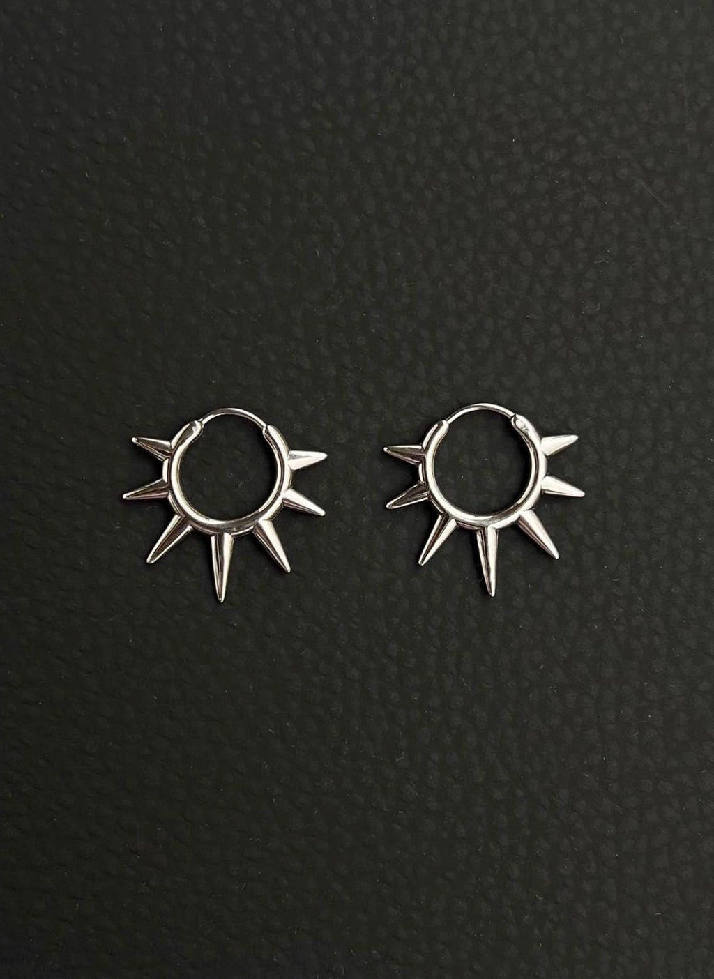 A pair of silver hoop earrings with a sunburst design. Each earring has a circular hoop with multiple pointed spikes radiating outwards. Handmade stainless steel earrings with a geometric sun design.