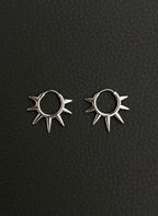 A pair of silver hoop earrings with a sunburst design. Each earring has a circular hoop with multiple pointed spikes radiating outwards. Handmade stainless steel earrings with a geometric sun design.