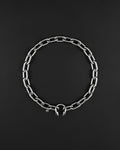 stainless steel Silver chunky heavy thick chain necklace. The necklace is composed of linked segments and a piercing barbel clasp with two spiked ends. The jewellery is set against a dark backdrop.