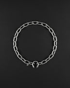stainless steel Silver chunky heavy thick chain necklace. The necklace is composed of linked segments and a piercing barbel clasp with two spiked ends. The jewellery is set against a dark backdrop.