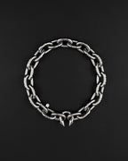 A stainless steel silver chunky heavy thick industrial chain necklace. The necklace has two pointed spikes at the clasp, the clasp is a piercing barbel. The jewellery is displayed on a black surface.