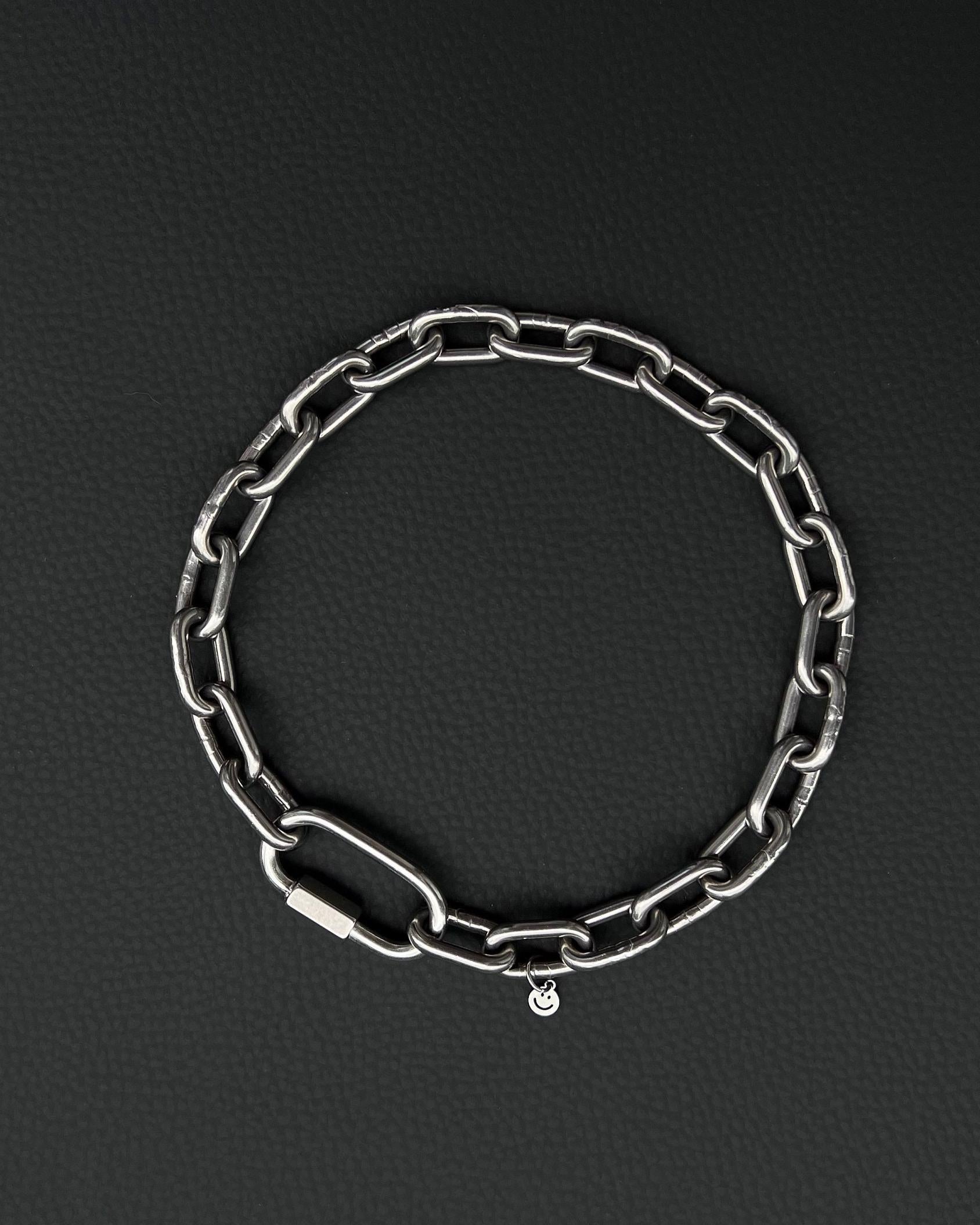 A handmade silver industrial chain necklace with large rectangular links. The necklace is made of stainless steel. The necklace is made from thick 4mm chain. The necklace includes a quick link carabiner and a smiley pendant.