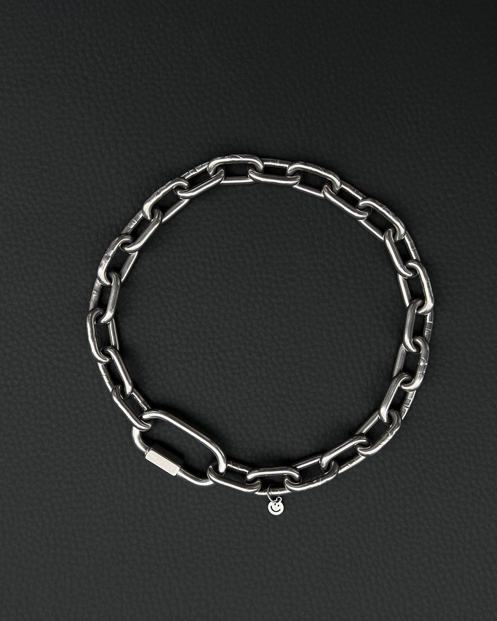 A handmade silver industrial chain necklace with large rectangular links. The necklace is made of stainless steel. The necklace is made from thick 4mm chain. The necklace includes a quick link carabiner and a smiley pendant. queer aesthetics