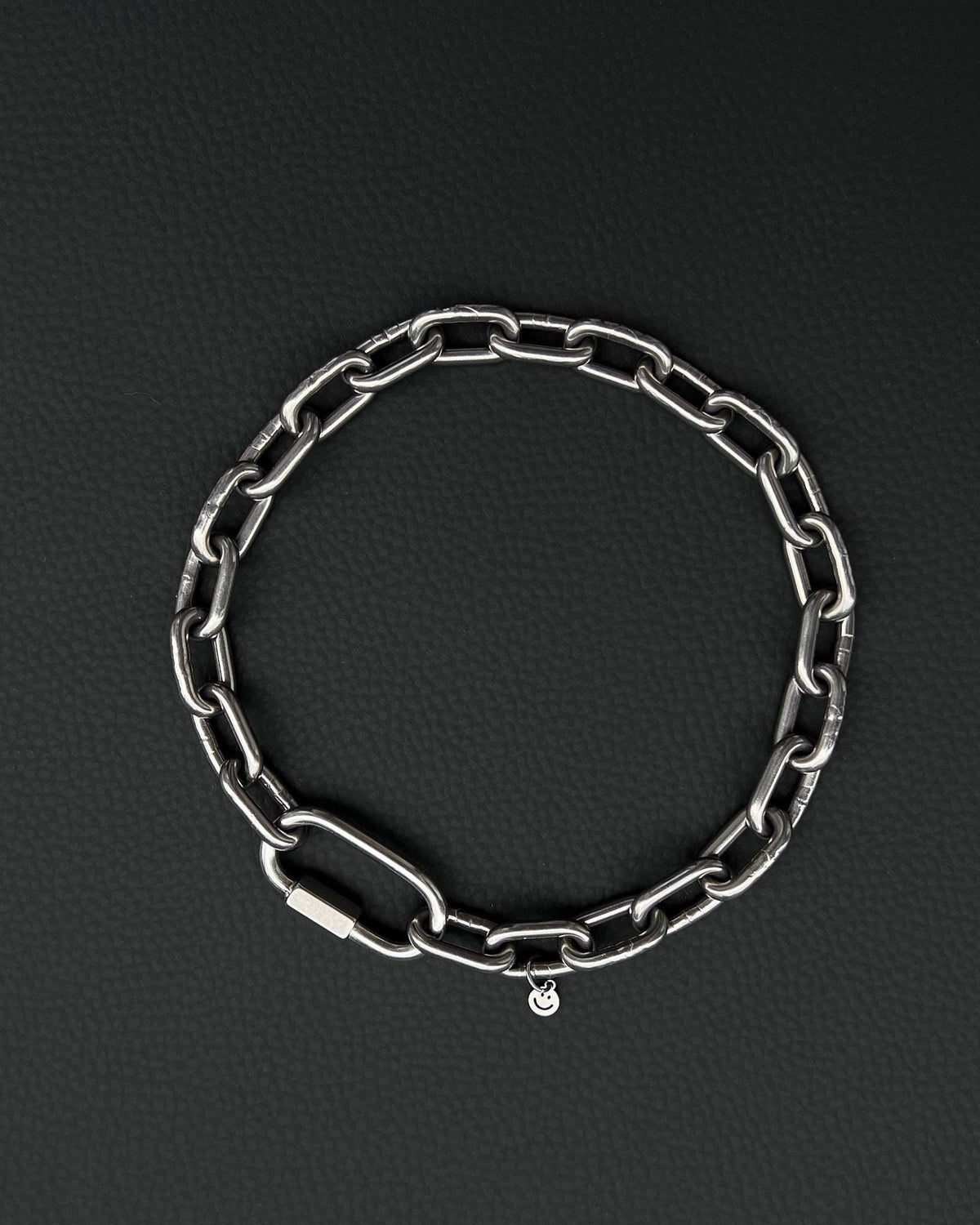 A handmade silver industrial chain necklace with large rectangular links. The necklace is made of stainless steel. The necklace is made from thick 4mm chain. The necklace includes a quick link carabiner and a smiley pendant. queer aesthetics