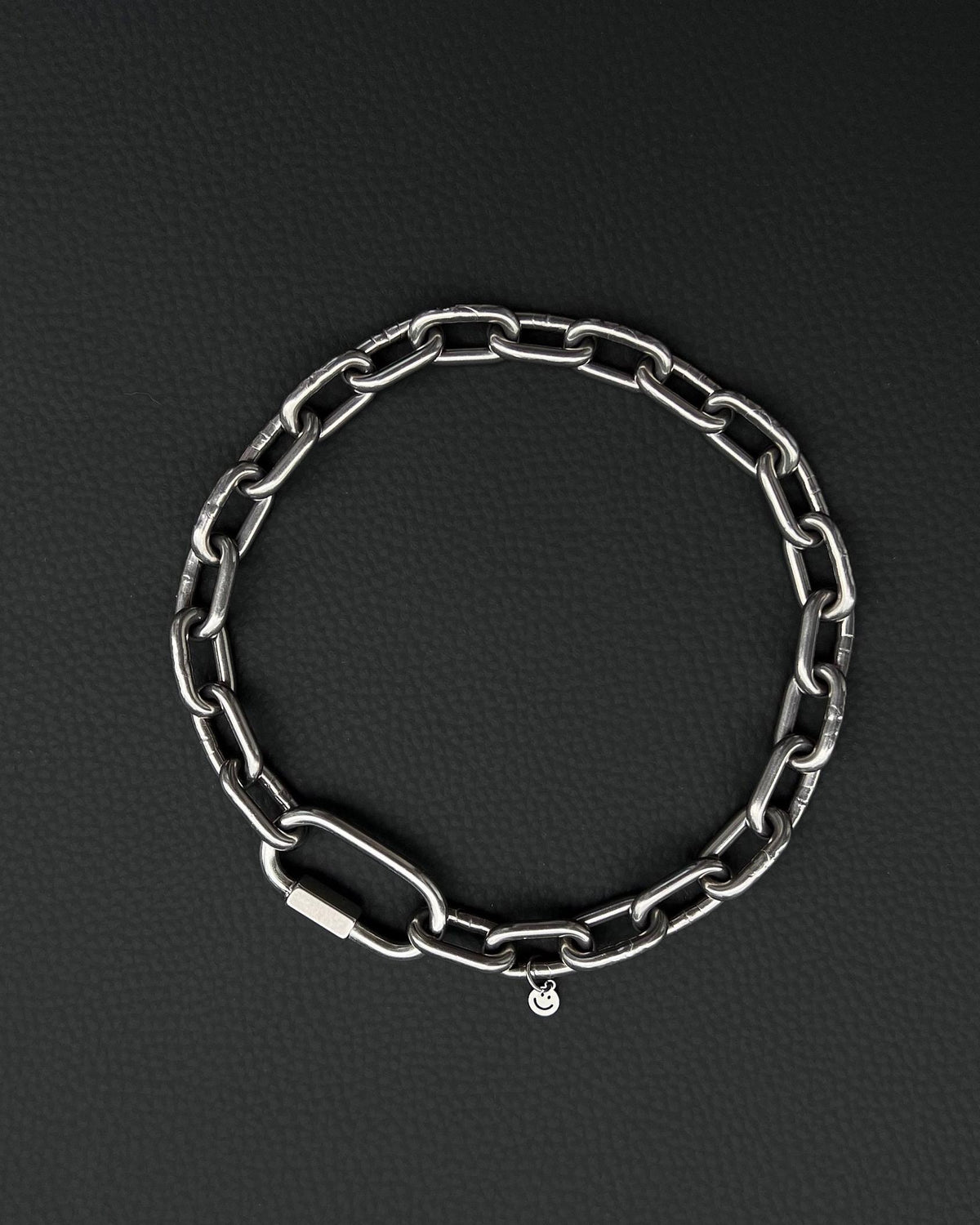 A handmade silver industrial chain necklace with large rectangular links. The necklace is made of stainless steel. The necklace is made from thick 4mm chain. The necklace includes a quick link carabiner and a smiley pendant. queer aesthetics