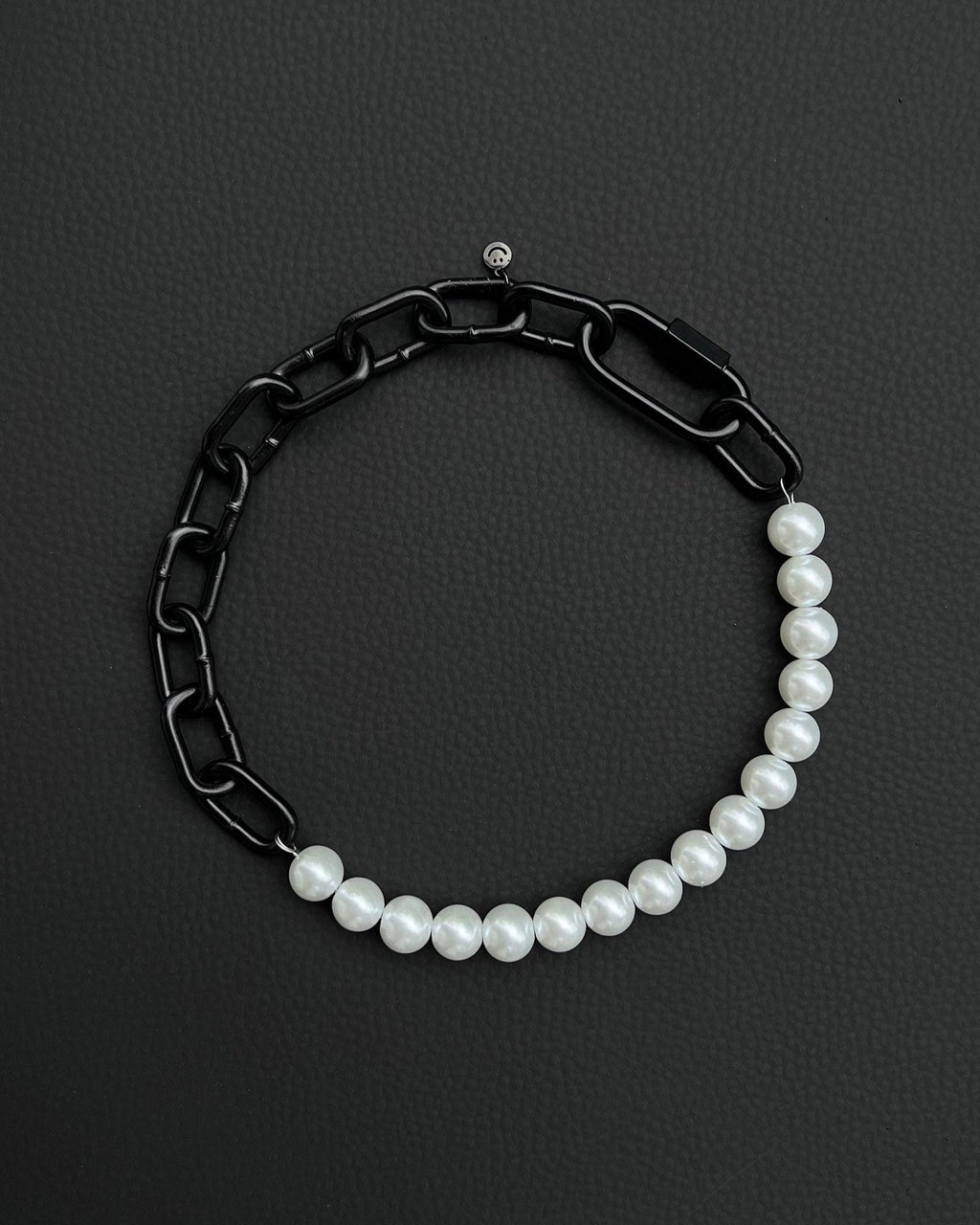 A handmade black industrial chain necklace with large, chunky, rectangular links. The necklace is made of metal steel. The necklace is made half-half from thick 4mm chain and 12mm glass white pearl beads. The necklace includes a black quick link carabiner and a smiley pendant.