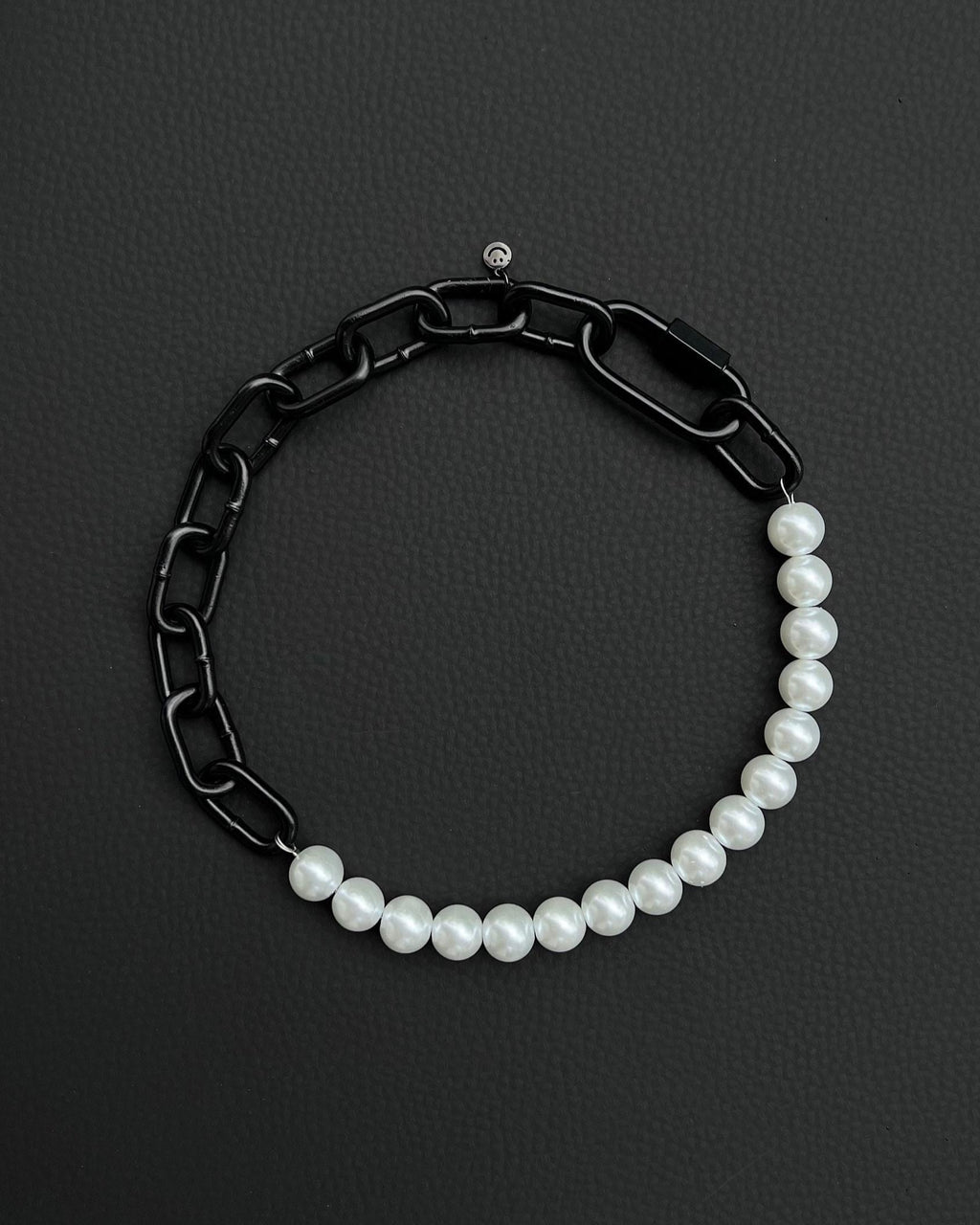 A handmade black industrial chain necklace with large, chunky, rectangular links. The necklace is made of stainless steel. The necklace is made half-half from thick 4mm chain and 12mm glass white pearl beads. The necklace includes a black quick link carabiner and a smiley pendant.