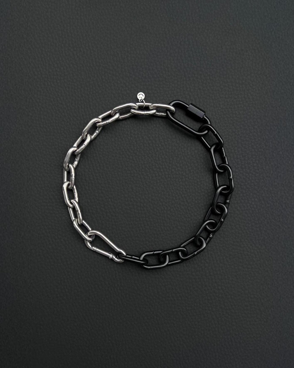 A two-tone stainless steel metal chunky heavy chain necklace. One half is silver, the other black. The necklace is made of interlocking chain links and has a small clasp. The background is a dark, textured surface.