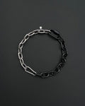A two-tone stainless steel metal chunky heavy chain necklace. One half is silver, the other black. The necklace is made of interlocking chain links and has a small clasp. The background is a dark, textured surface.