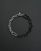 A two-tone stainless steel metal chunky heavy chain necklace. One half is silver, the other black. The necklace is made of interlocking chain links and has a small clasp. The background is a dark, textured surface.