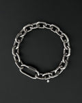A thick silver stainless steel chain necklace with a large carabiner clasp. The choker is made of thick, oversized, interlocking links and has a small charm with a smiley face. The necklace is displayed on a black surface. the chain is made of 6mm thick links. queer aesthetics