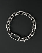 A thick silver stainless steel chain necklace with a large carabiner clasp. The choker is made of thick, oversized, interlocking links and has a small charm with a smiley face. The necklace is displayed on a black surface. the chain is made of 6mm thick links. queer aesthetics
