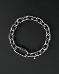 A thick silver stainless steel chain necklace with a large carabiner clasp. The choker is made of thick, oversized, interlocking links and has a small charm with a smiley face. The necklace is displayed on a black surface.