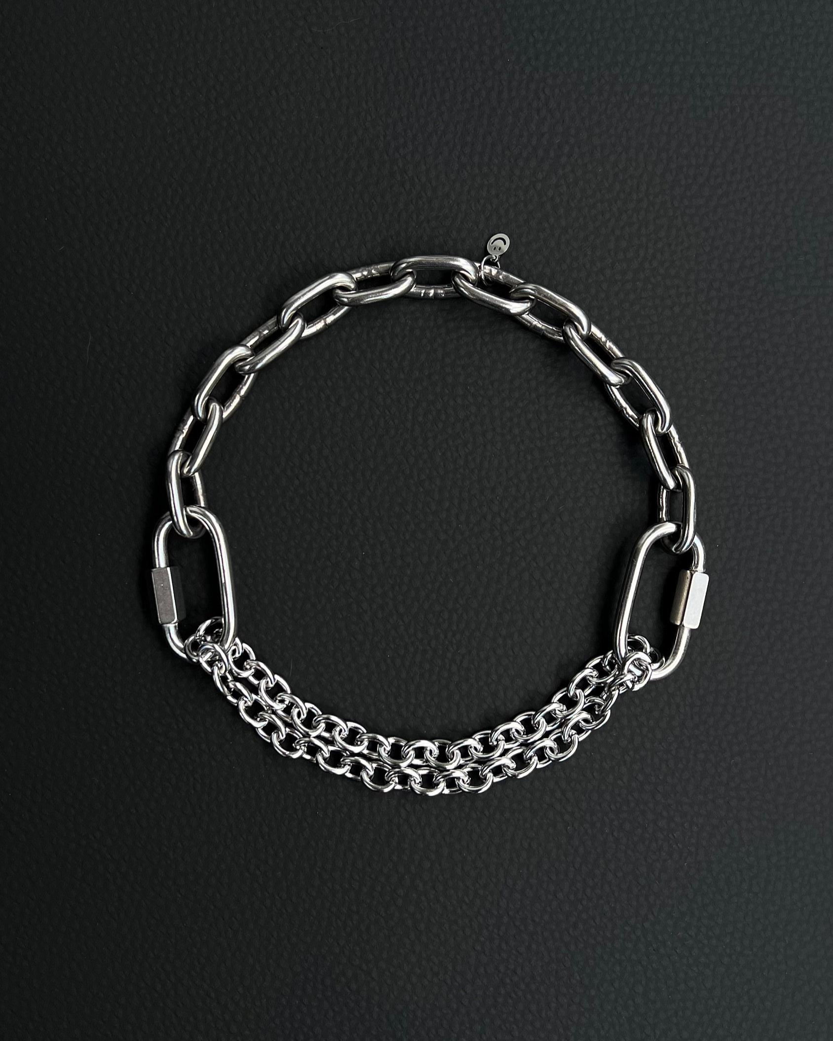 Handmade stainless steel martingale chain choker with two industrial chain types, two quick link clasps and a small smiley charm. Silver finish necklace photographed on a black background.