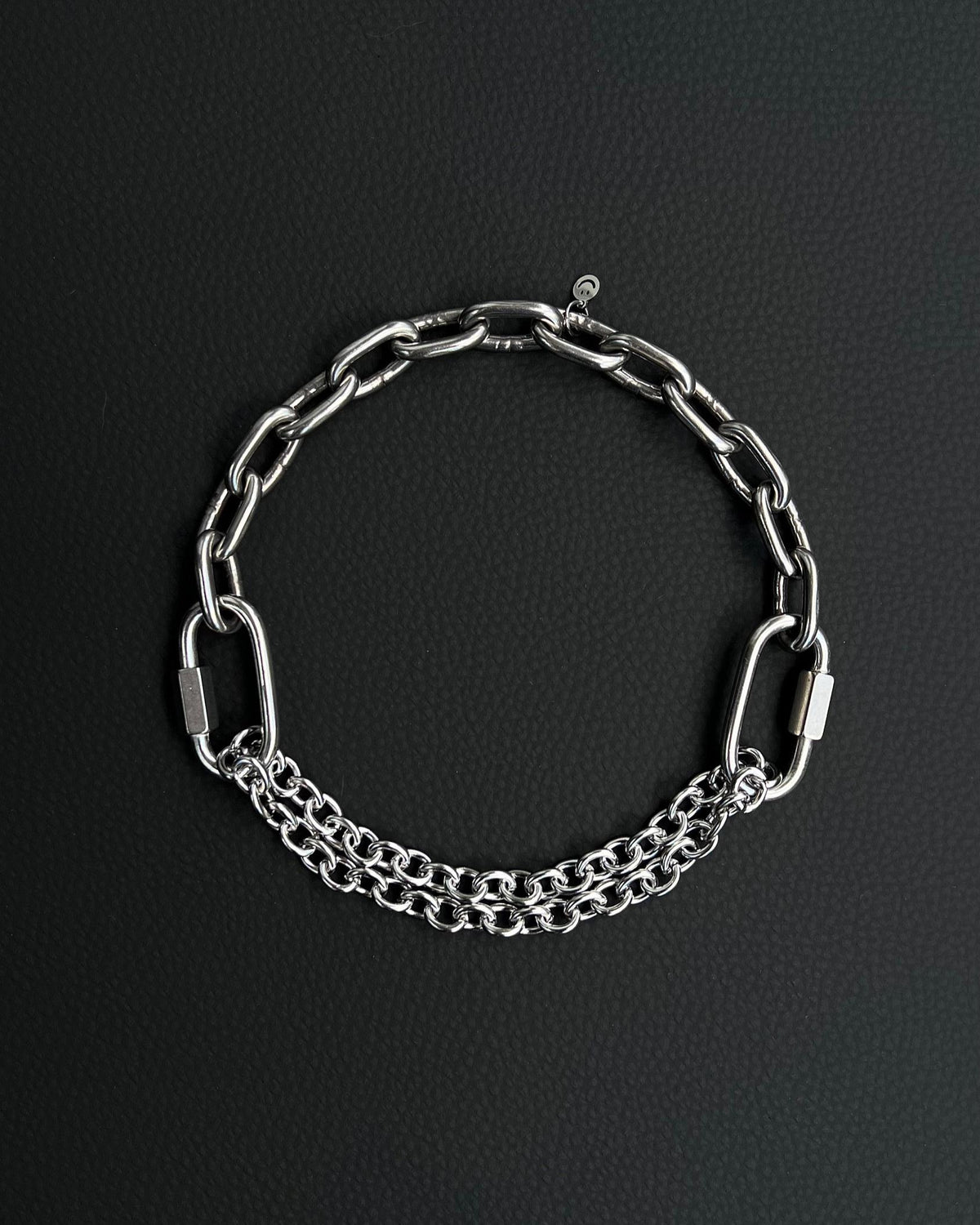 Handmade stainless steel martingale chain choker with two industrial chain types, two quick link clasps and a small smiley charm. Silver finish necklace photographed on a black background.