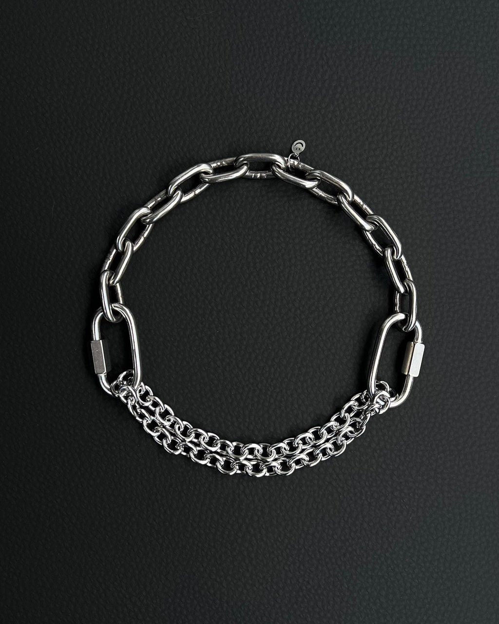 Handmade stainless steel martingale chain choker with two industrial chain types, two quick link clasps and a small smiley charm. Silver finish necklace photographed on a black background.