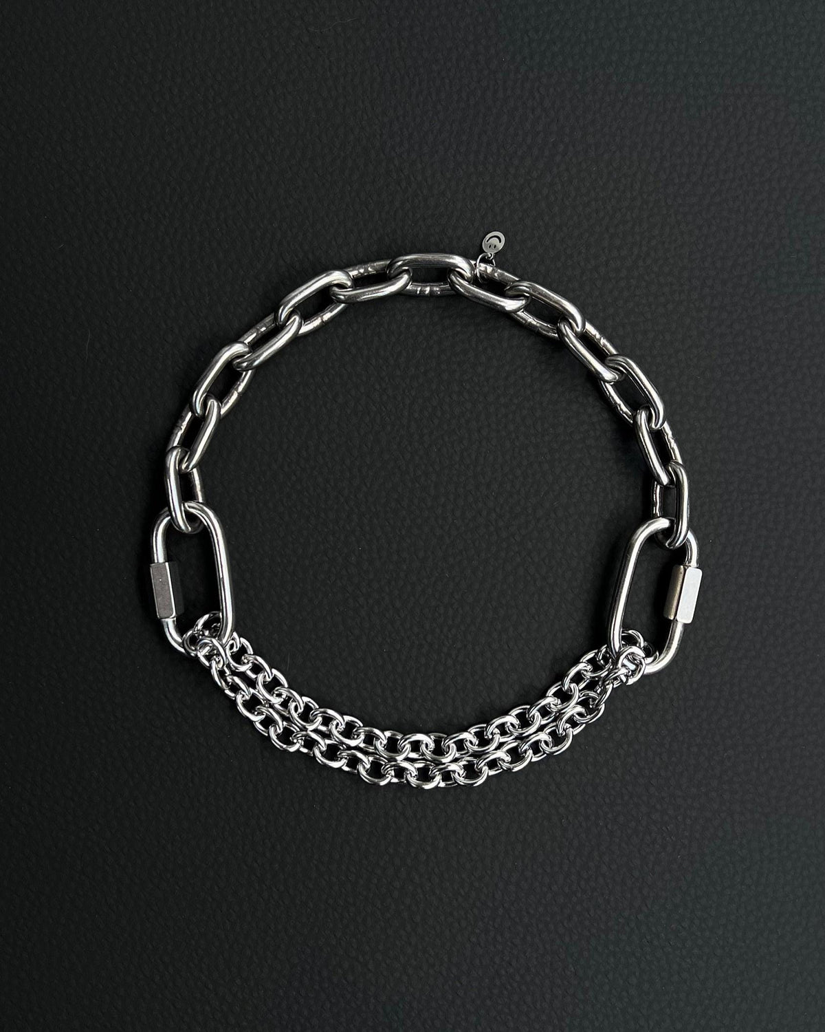 Handmade stainless steel martingale chain choker with two industrial chain types, two quick link clasps and a small smiley charm. Silver finish necklace photographed on a black background.