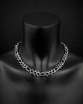 A stainless steel silver chain necklace with a chunky, textured design. The necklace is displayed on a black mannequin. The chain links are thick and feature small, decorative studs. The overall aesthetic is bold and modern.