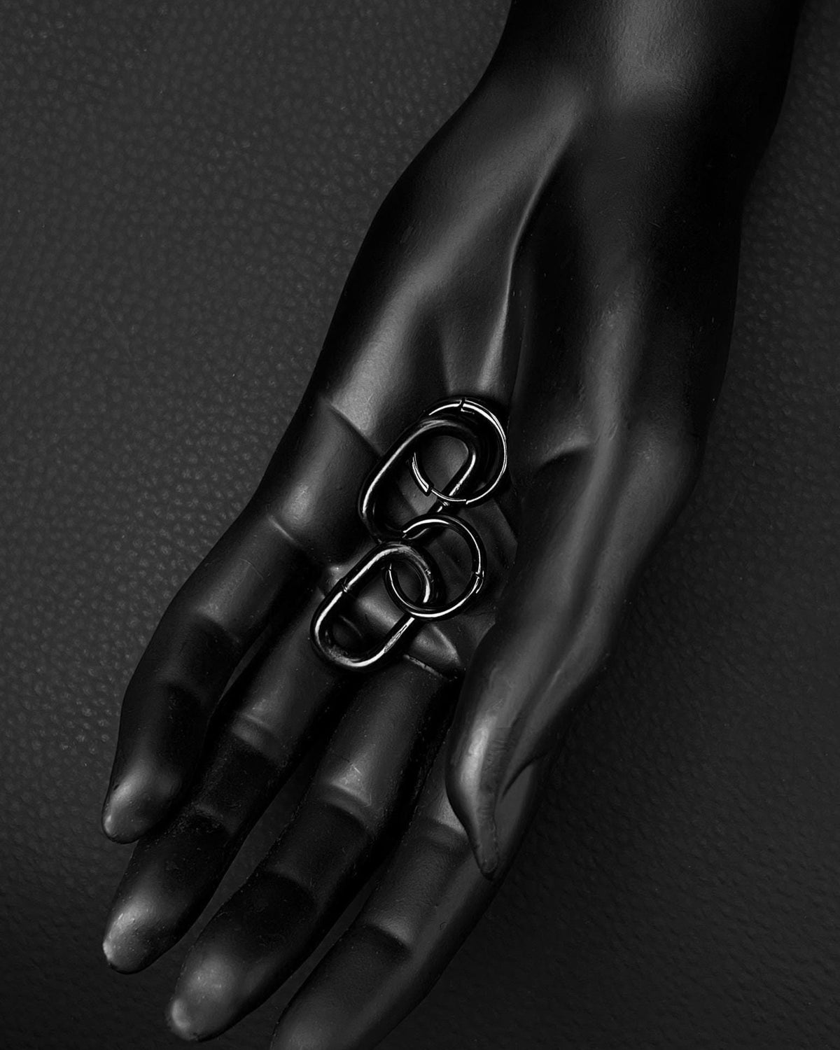 A black stainless steel earring with a hoop and oval industrial chain link The background is a dark, textured surface.