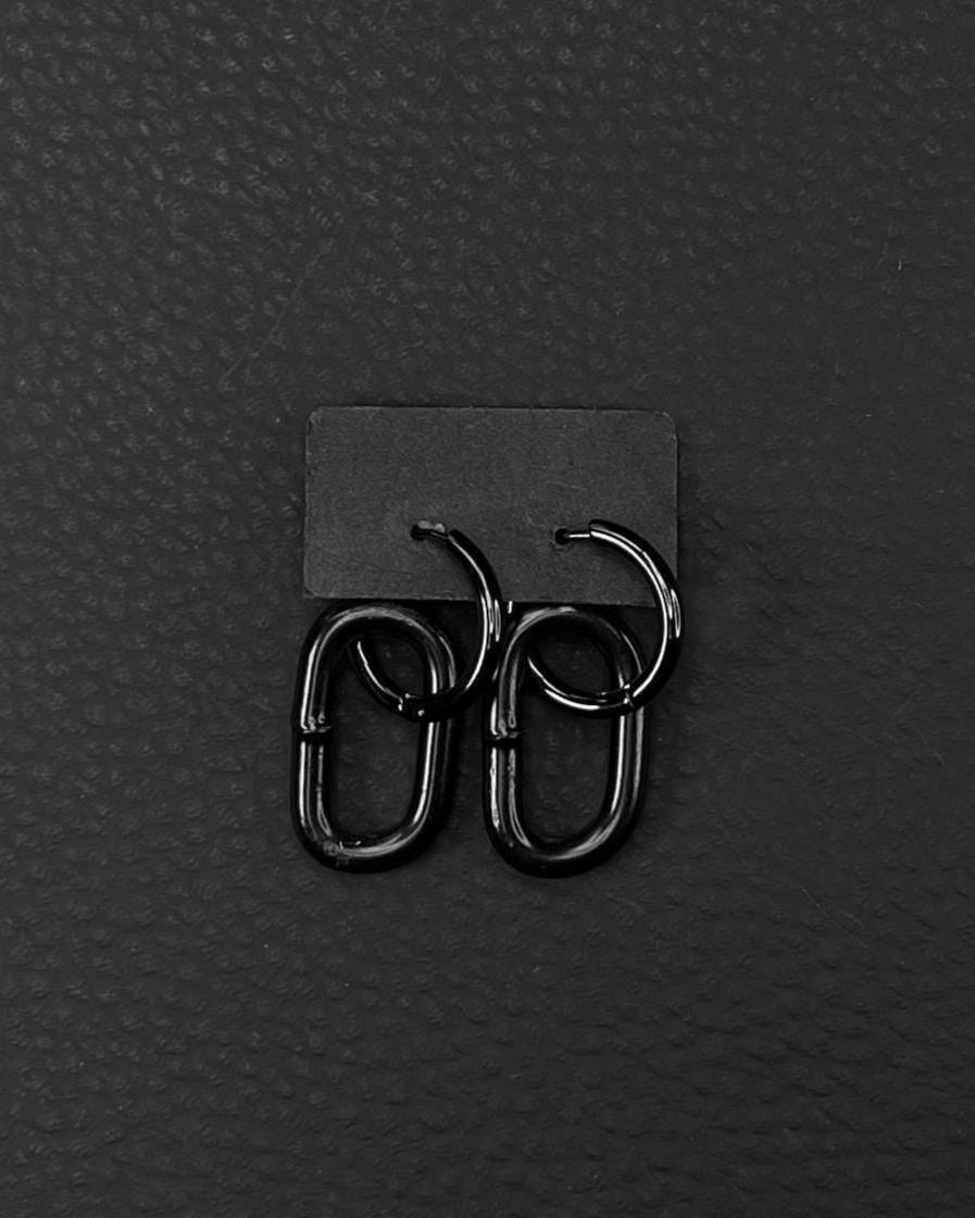 A pair of black stainless steel earrings with a distinctive design. Earrings are made of black industrail chain link and a hoop. Each earring has a small hoop linked to a larger, oval-shaped link. The earrings are presented on a black card against a black backdrop, creating a sleek, modern aesthetic.