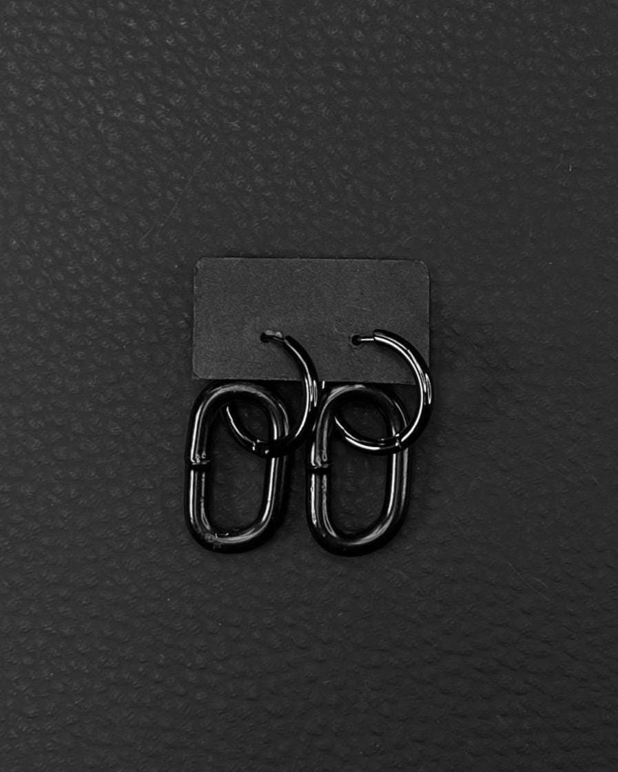 A pair of black stainless steel earrings with a distinctive design. Earrings are made of black industrail chain link and a hoop. Each earring has a small hoop linked to a larger, oval-shaped link. The earrings are presented on a black card against a black backdrop, creating a sleek, modern aesthetic.