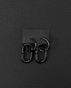A pair of black stainless steel earrings with a distinctive design. Earrings are made of black industrail chain link and a hoop. Each earring has a small hoop linked to a larger, oval-shaped link. The earrings are presented on a black card against a black backdrop, creating a sleek, modern aesthetic.
