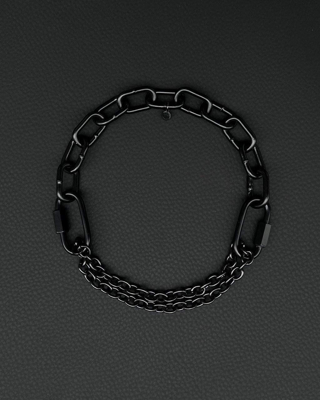Handmade  steel martingale chain choker with two industrial chain types, two quick link clasps and a small smiley charm. Black finish necklace photographed on a black background.
