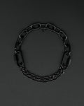 Handmade  steel martingale chain choker with two industrial chain types, two quick link clasps and a small smiley charm. Black finish necklace photographed on a black background.