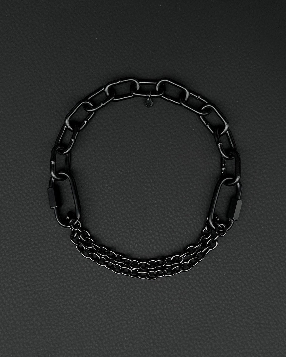 Chunky, black, steel martingale chain choker with two industrial chain types, a thick 4mm chain and two strands of a thinner black chain, two quick link clasps and a small smiley charm. Black finish necklace photographed on a black background.