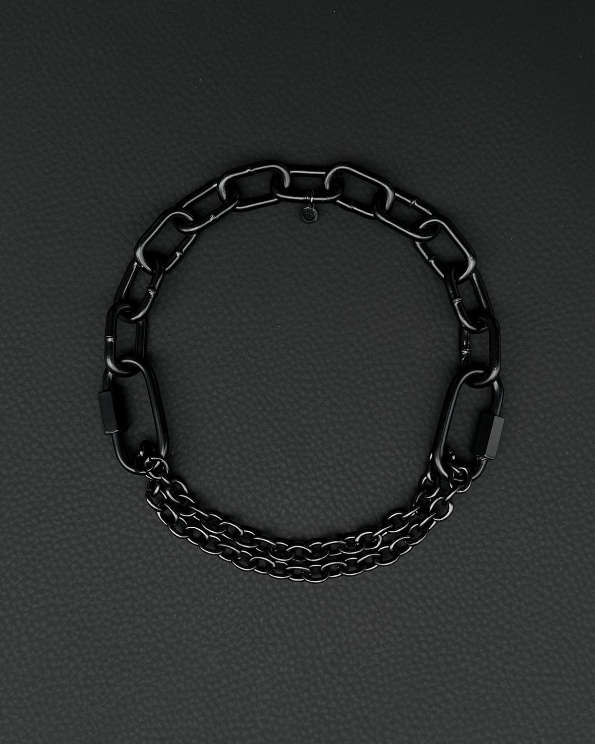 Chunky handmade  steel martingale chain choker with two industrial chain types, two quick link clasps and a small smiley charm. Black finish necklace photographed on a black background.