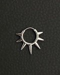 A silver-toned stainless steel circular hoop earring featuring a series of seven pointed spikes extending outwards from the outer edge of the ring. the earring looks like a symbolic sun, sun rays. The metal has a polished, reflective finish, and the design forms a sunburst or star-like shape.
