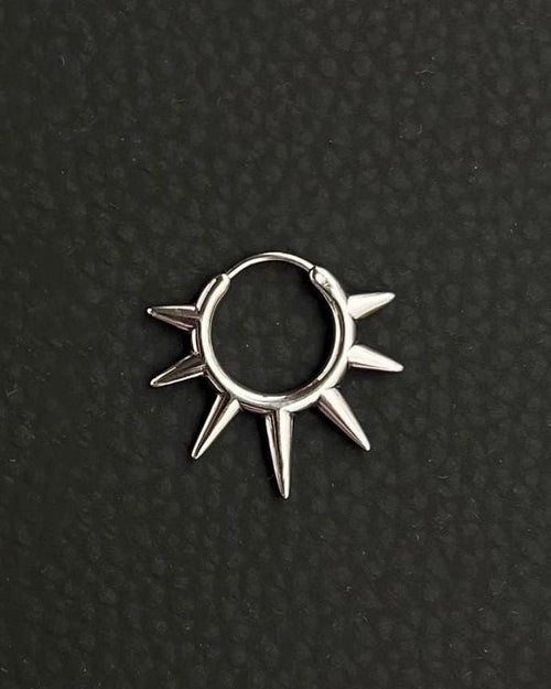A silver-toned stainless steel circular hoop earring featuring a series of seven pointed spikes extending outwards from the outer edge of the ring. the earring looks like a symbolic sun, sun rays. The metal has a polished, reflective finish, and the design forms a sunburst or star-like shape.
