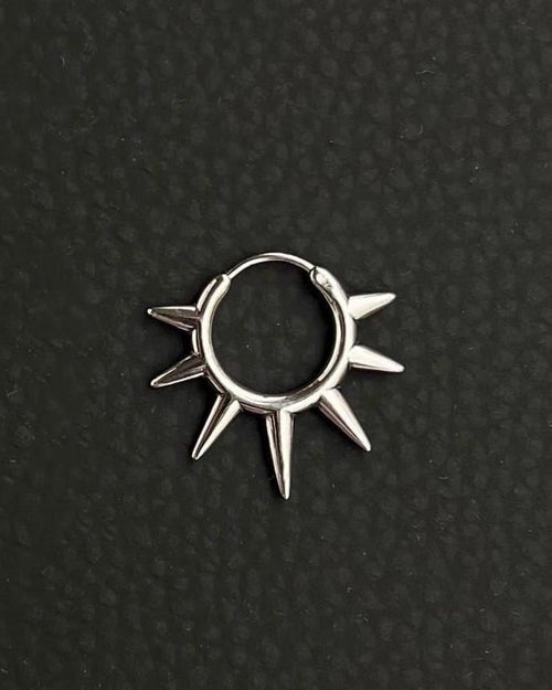 A silver-toned stainless steel circular hoop earring featuring a series of seven pointed spikes extending outwards from the outer edge of the ring. the earring looks like a symbolic sun, sun rays. The metal has a polished, reflective finish, and the design forms a sunburst or star-like shape.