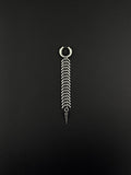 A silver-toned stainless steel hoop earring featuring a long, dangling chain composed of multiple curved, fishbone-like metal links. The chain terminates in a sharp, conical spike pendant, creating a vertical, articulated design with a polished metallic finish.