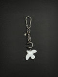 A silver-toned stainless steel metal keyring featuring a carabiner clip, a short chainmaille chain with circular links, a small smiley face charm, a curved metal barbel piercing earring with two pointed spikes, and a white glass peace dove bird-shaped pendant with etched wing details.