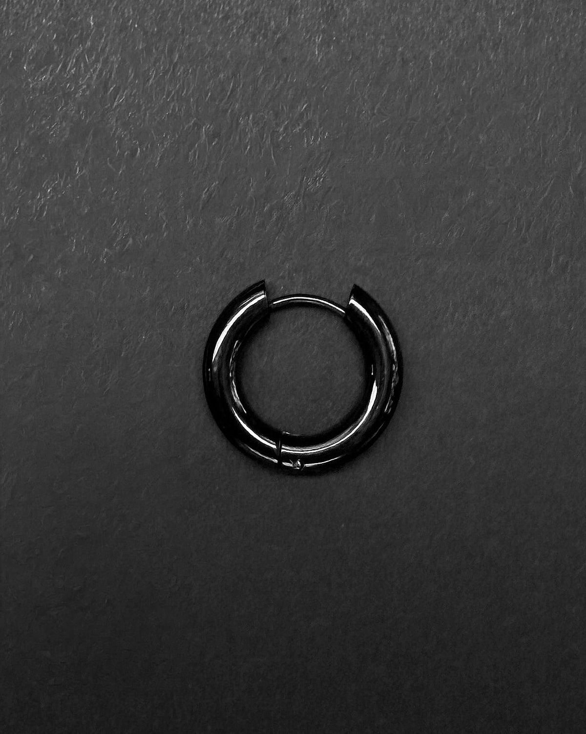 A single stainless steel circular thick big hoop earring with a polished black finish. The earring features a hinged closure mechanism with a thin post that secures into the main hoop body, creating a continuous, smooth, and rounded silhouette for the piece.