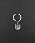 A silver-toned stainless steel  metal hoop earring featuring a single clear, faceted, irregular-shaped quartz crystal pendant hanging from the bottom. The earring has a smooth, polished finish and a hinged closure mechanism at the top of the circular hoop.