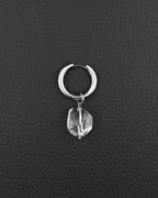 A silver-toned stainless steel  metal hoop earring featuring a single clear, faceted, irregular-shaped quartz crystal pendant hanging from the bottom. The earring has a smooth, polished finish and a hinged closure mechanism at the top of the circular hoop.