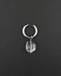 A silver stainless steel hoop earring featuring a single clear, faceted, irregular-shaped quartz crystal pendant hanging from the bottom. The earring has a smooth, polished finish and a hinged closure mechanism at the top of the circular hoop.