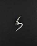 A polished silver-tone stainless steel brooch featuring a sleek, abstract, curved design that resembles a stylised letter S. The piece has a smooth, reflective surface with sharp, pointed ends and a fluid, organic shape that tapers at both extremities.