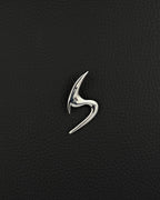 A polished silver-tone stainless steel brooch featuring a sleek, abstract, curved design that resembles a stylised letter S. The piece has a smooth, reflective surface with sharp, pointed ends and a fluid, organic shape that tapers at both extremities.