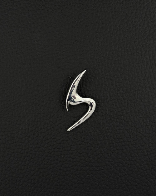 A polished silver-tone stainless steel brooch featuring a sleek, abstract, curved design that resembles a stylised letter S. The piece has a smooth, reflective surface with sharp, pointed ends and a fluid, organic shape that tapers at both extremities.