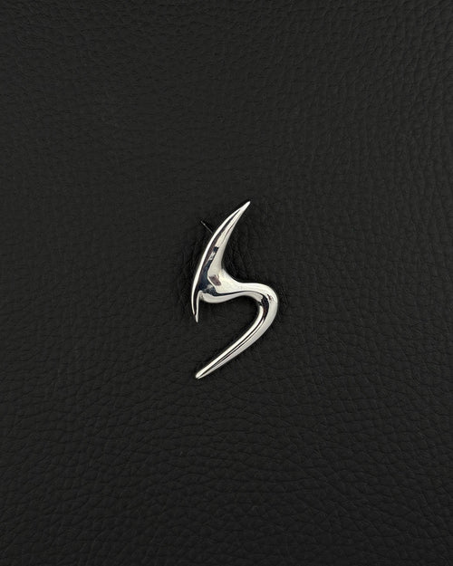 A polished silver-tone stainless steel brooch featuring a sleek, abstract, curved design that resembles a stylised letter S. The piece has a smooth, reflective surface with sharp, pointed ends and a fluid, organic shape that tapers at both extremities.