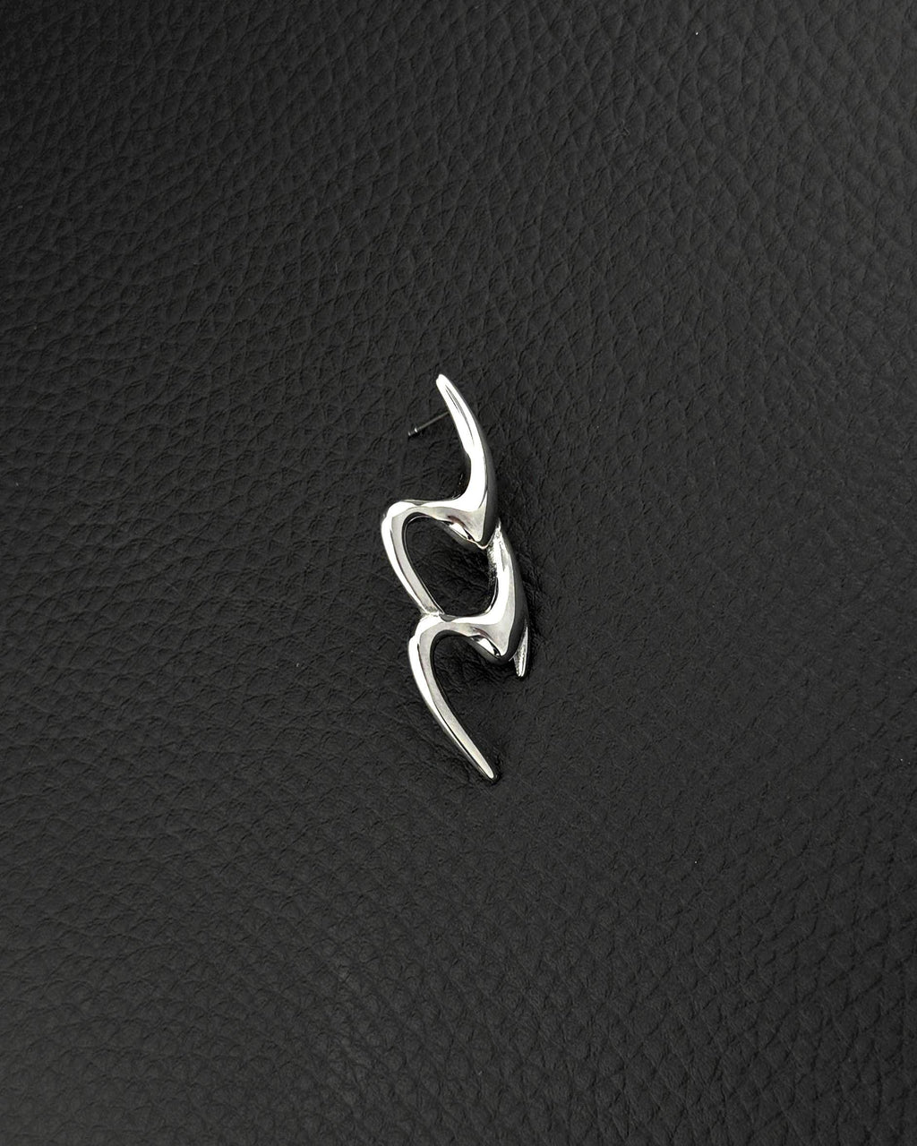 A single silver-toned stainless steel earring featuring an elongated, fluid, and abstract shape with smooth, polished surfaces in the cyber sigilism style. The design consists of two interconnected, curved segments that create an open, organic form with a post backing.