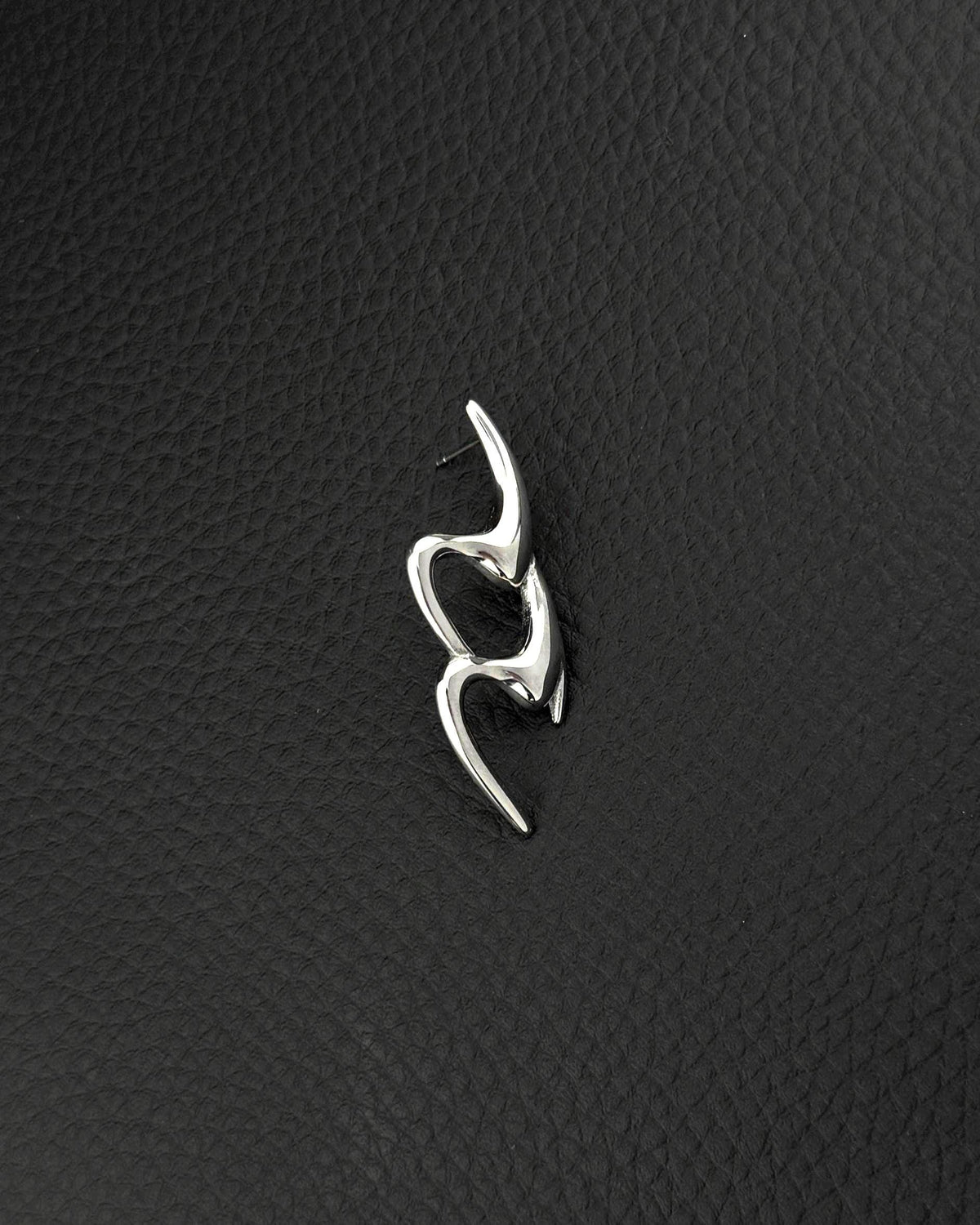 A single silver-toned stainless steel earring featuring an elongated, fluid, and abstract shape with smooth, polished surfaces in the cyber sigilism style. The design consists of two interconnected, curved segments that create an open, organic form with a post backing.