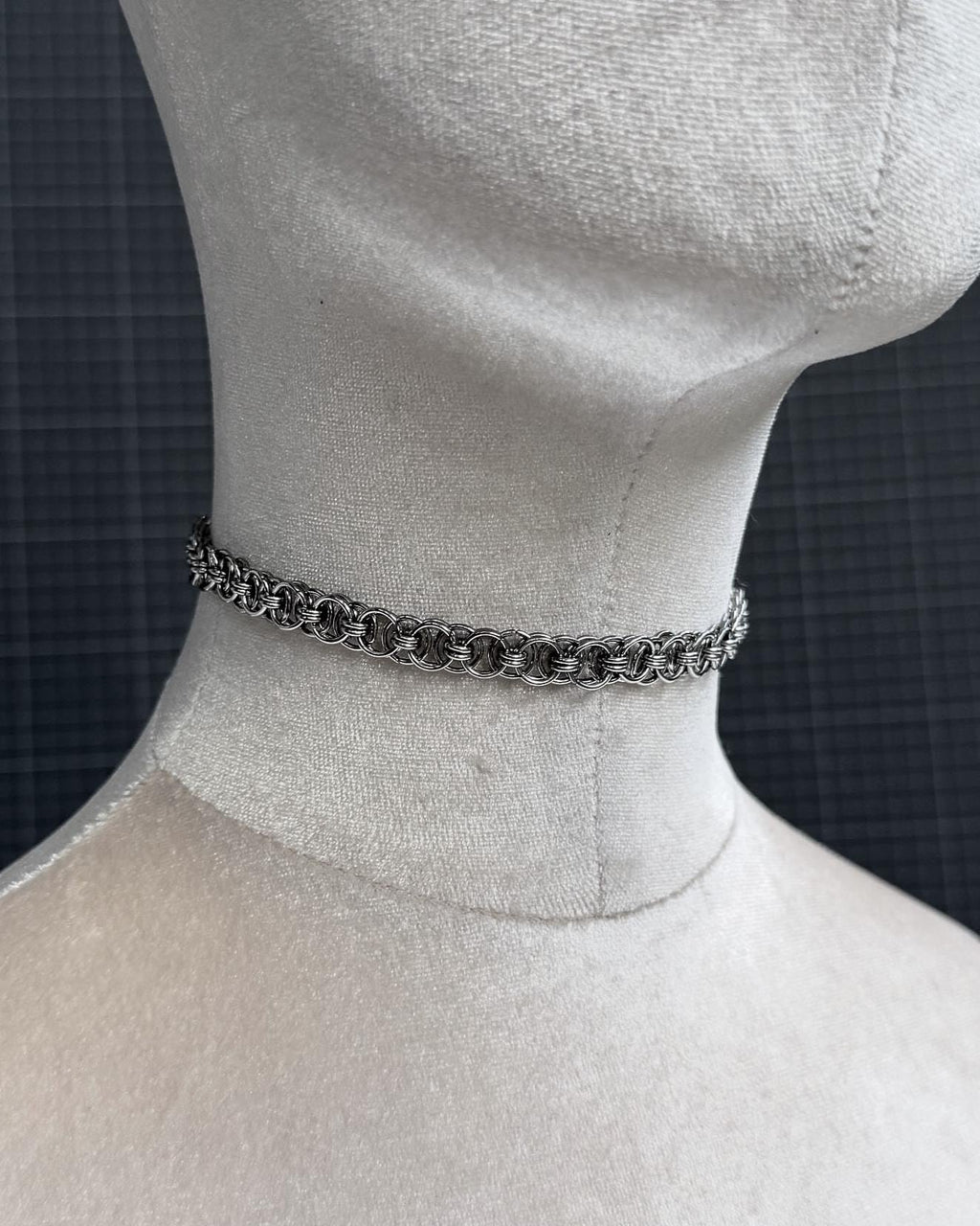A silver-toned stainless steel chainmail tattoo choker necklace featuring a repeating pattern of interlocking metal rings. The necklace is constructed from small, circular links that create a textured, woven appearance around the neck of the display form.