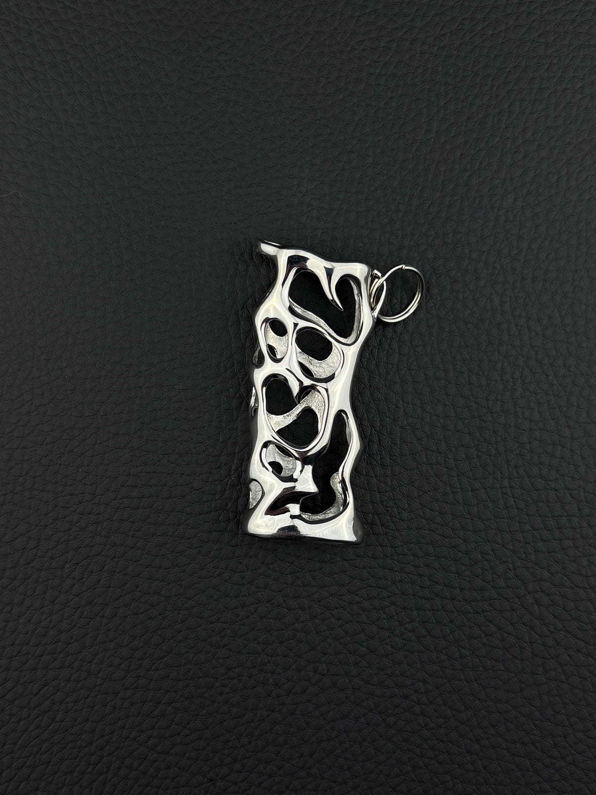 A silver-toned stainless steel pendant lighter sleeve featuring an elongated, irregular rectangular shape with a complex, organic cutout pattern throughout its surface. The metal has a polished, reflective finish and includes a small circular jump ring attached at the top. cyber sigilism style