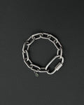 A silver-toned stainless steel chunky chain bracelet composed of thick, interlocking rectangular links. The bracelet features a large, elongated carabiner-style clasp and a small, circular charm engraved with a simple smiley face icon.