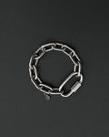 A silver-toned stainless steel chunky chain bracelet composed of thick, interlocking rectangular links. The bracelet features a large, elongated carabiner-style clasp and a small, circular charm engraved with a simple smiley face icon.