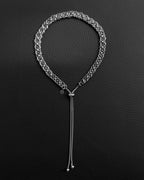 A silver-toned chainmail necklace featuring a circular link pattern. The necklace includes an adjustable sliding bead mechanism with two dangling box chains and a small circular charm embossed with a smiley face icon.